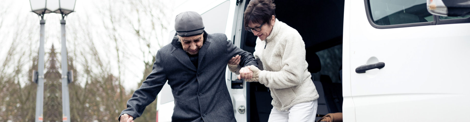 Nurse helping senior man exit a van and get to his wheelchair